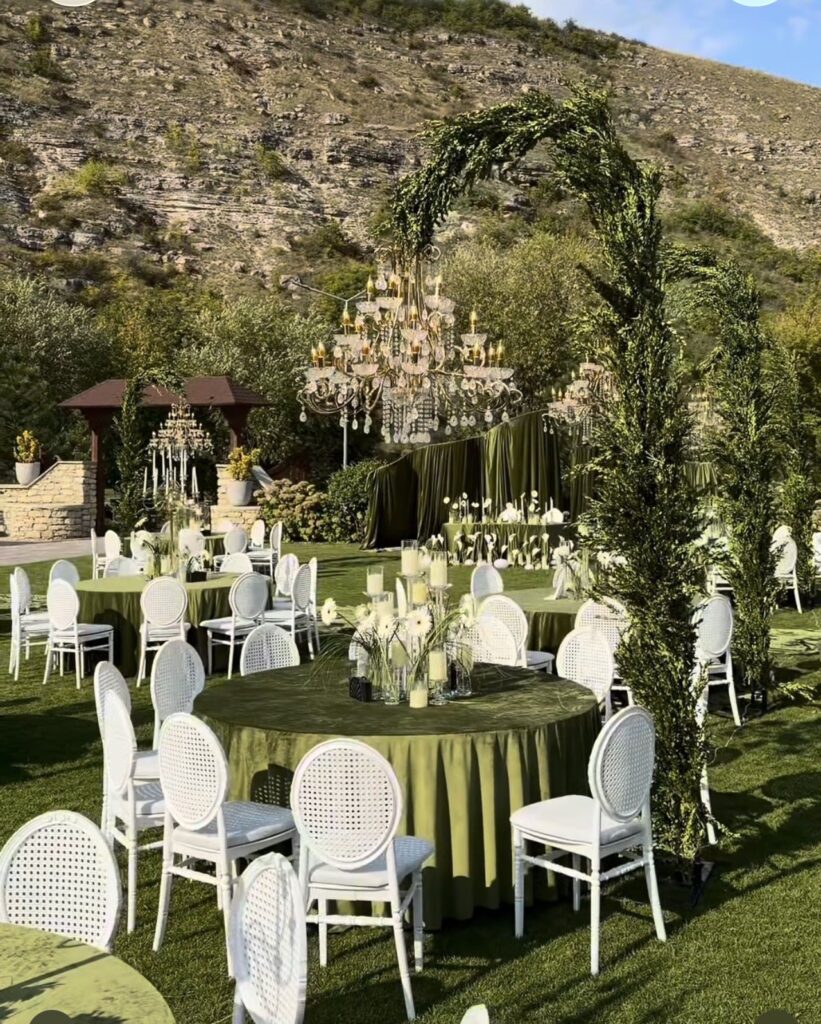 Garden reception with green linens, white chairs and chandeliers by Fems Events